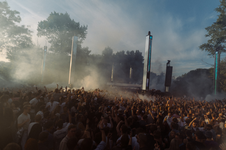 Large outdoor concert crowd in front of a stage with tall vertical LED towers and smoke in the air.