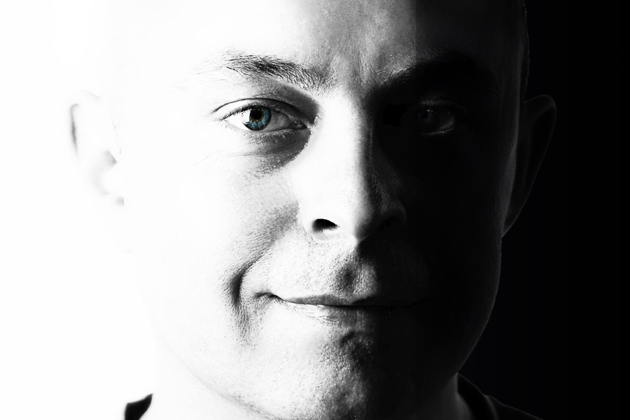 Close-up portrait of a man's face in black and white, with a blue eye visible on the bright side.