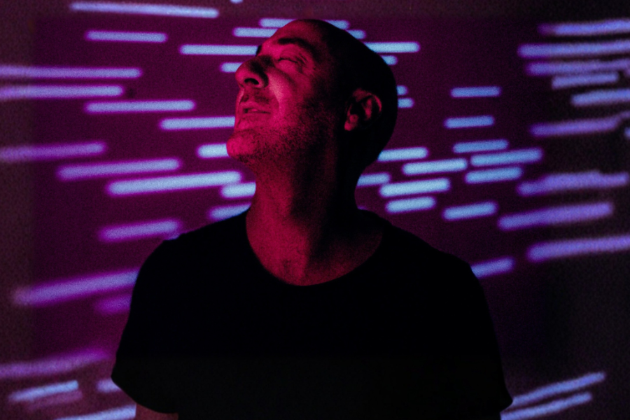 Portrait of a man in a black t-shirt, head tilted up, bathed in magenta/purple neon light streaks behind him.