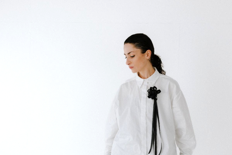 Woman in an oversized white shirt with a black bow and long tassels, looking downward.